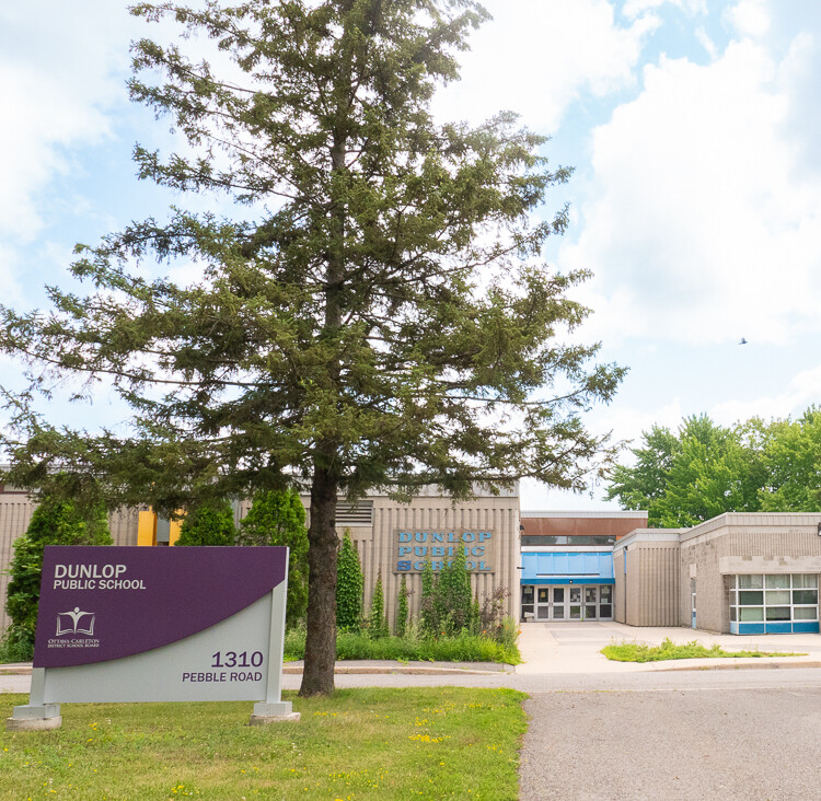 School Entrance with a long walkway, large trees and a dominate school sign.